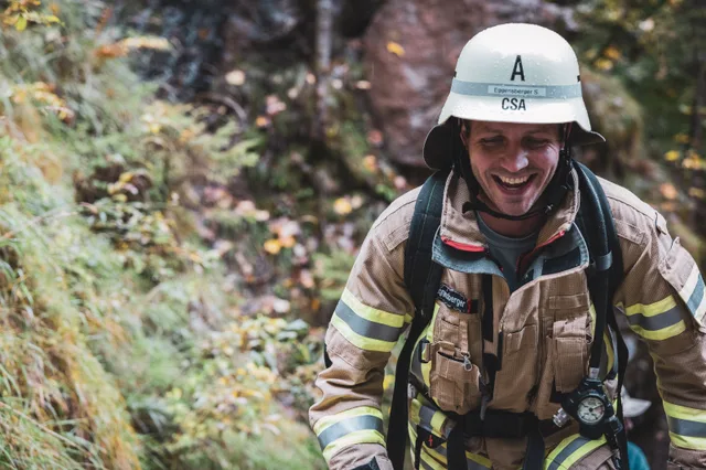Lächelnder Teilnehmer in beiger Einsatzkleidung auf den Metallstufen.