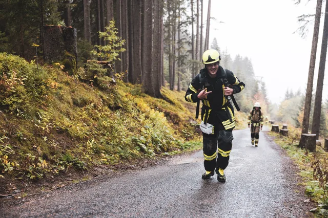 Lachender Teilnehmer mit gelbem Helm hält beim Aufstieg die Tragegurte.