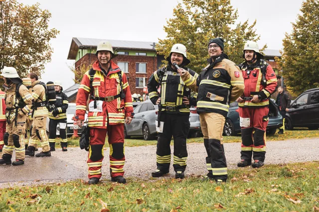 Lachende Teilnehmer in roter und schwarzer Einsatzkleidung.