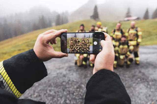 Ein Mobiltelefon zeigt das Gruppenbild der Teilnehmer vor dem Berghang.