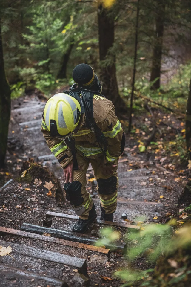 Teilnehmer in beiger Einsatzkleidung und gelbem Helm auf steilen Waldstufen.