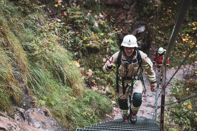 Lächelnder Teilnehmer in beiger Einsatzkleidung auf den Metallstufen.