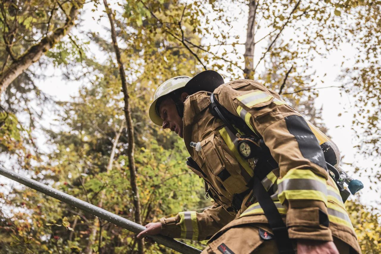 Feuerwehrmann in beiger Schutzkleidung steigt am Geländer entlang durch den herbstlichen Wald.