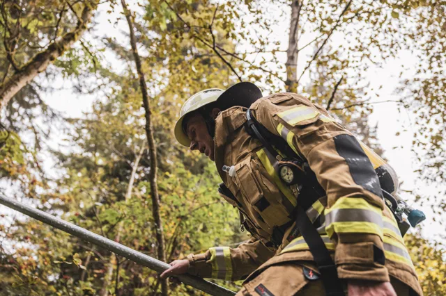 Feuerwehrmann in beiger Schutzkleidung steigt am Geländer entlang durch den herbstlichen Wald.