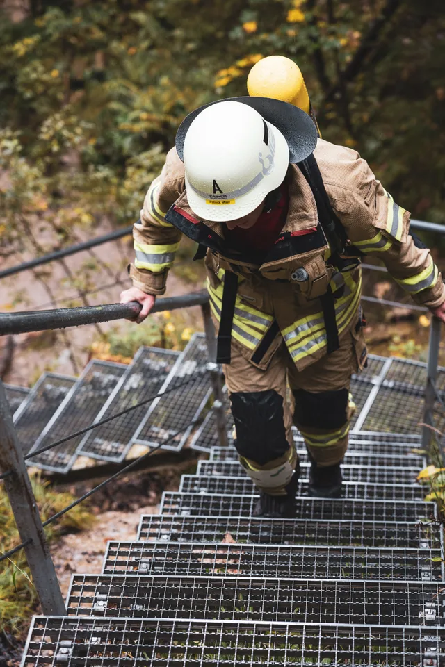 Teilnehmer in beiger Einsatzkleidung auf einer Metalltreppe, von oben gesehen.