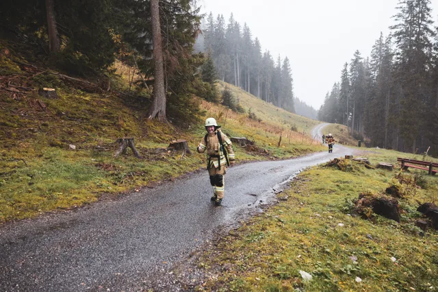 Teilnehmer auf der nassen Bergstraße zwischen Wiese und Wald.