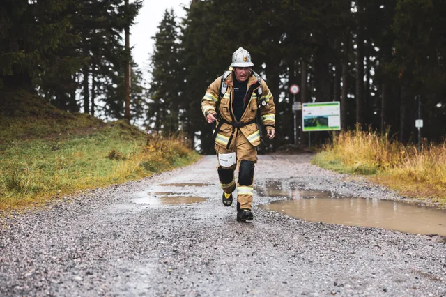 Teilnehmer in beiger Einsatzkleidung läuft über den nassen Schotter ins Ziel.