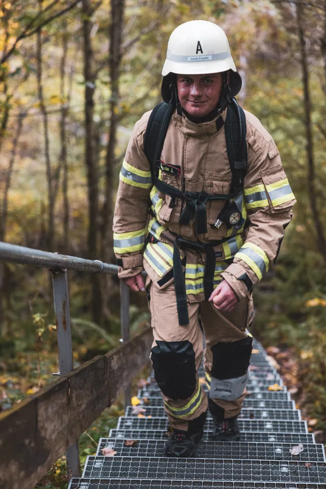 Teilnehmer mit weißem Helm und beiger Einsatzkleidung steigt eine lange Metalltreppe hinauf.