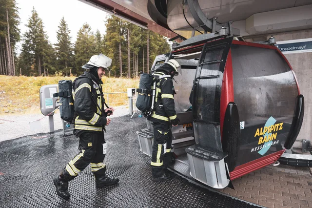 Teilnehmer mit Atemschutzgeräten steigen an der Bergstation in die Gondel.