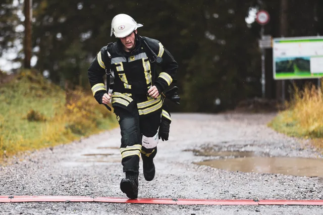 Teilnehmer in schwarzer Einsatzkleidung läuft über den nassen Schotter ins Ziel.