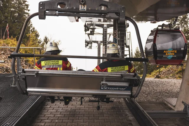 Teilnehmer mit gelben Helmen fahren im Sessellift.