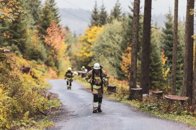 Teilnehmer in beiger Einsatzkleidung auf der nassen Bergstraße im Herbstwald.
