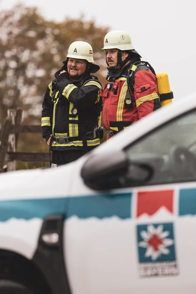 Zwei Teilnehmer mit weißen Helmen hinter einem Rettungsfahrzeug.
