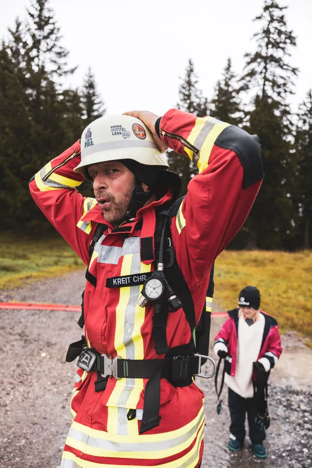 Teilnehmer in roter Einsatzkleidung hält lächelnd beide Hände an den Helm.
