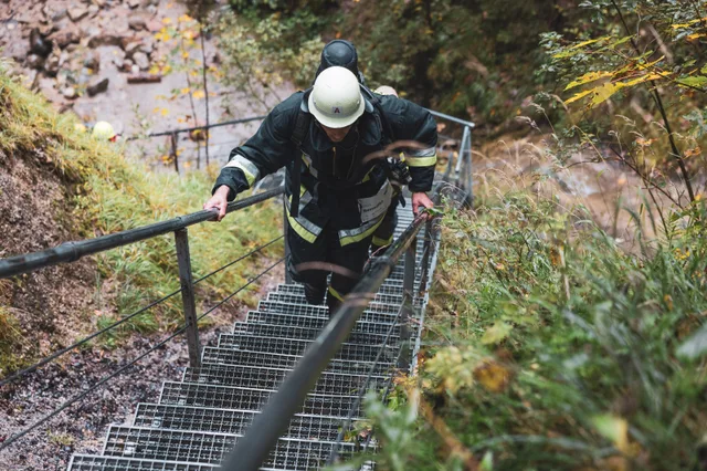 Teilnehmer in schwarzer Einsatzkleidung und weißem Helm steigt die Waldtreppe hinauf.