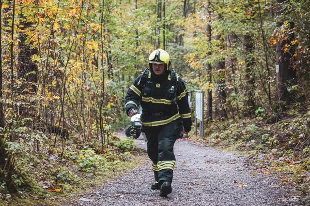 Teilnehmer in dunkler Einsatzkleidung und weißem Helm auf dem Waldweg.