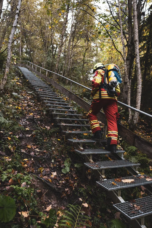 Teilnehmer in roter Einsatzkleidung auf einer steilen Metalltreppe.