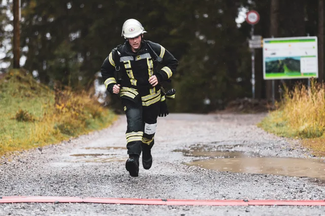 Teilnehmer in schwarzer Einsatzkleidung läuft über den nassen Schotter ins Ziel.