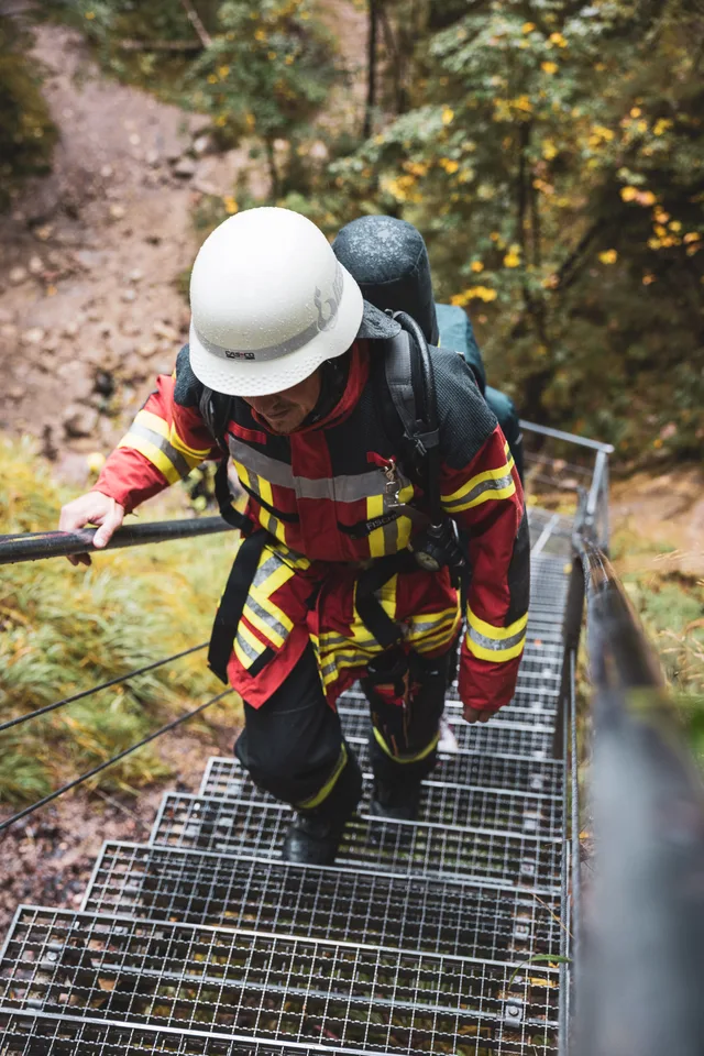Teilnehmer in roter Einsatzkleidung und weißem Helm auf einer Metalltreppe.