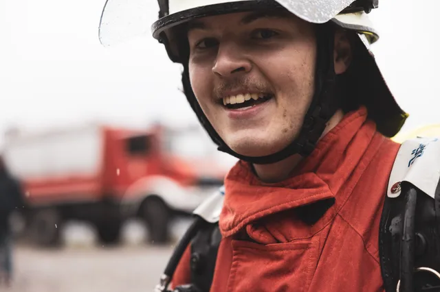 Lächelnder Teilnehmer mit weißem Helm und roter Jacke im Ziel.