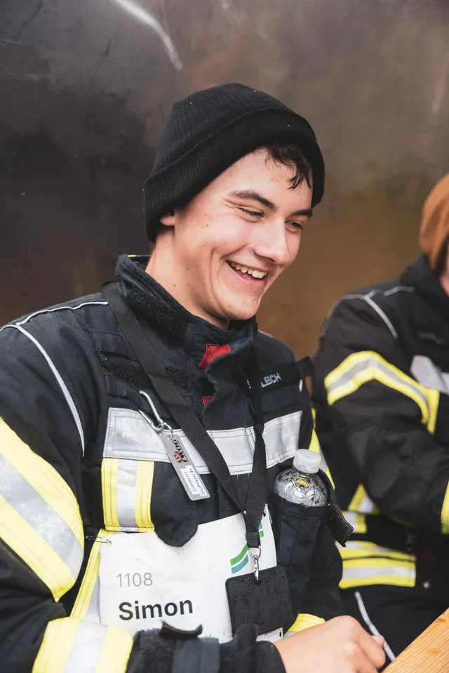 Lachender Teilnehmer mit schwarzer Mütze und Startnummer auf der Einsatzjacke.
