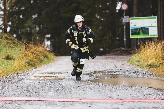 Teilnehmer in schwarzer Einsatzkleidung läuft über den nassen Schotter ins Ziel.