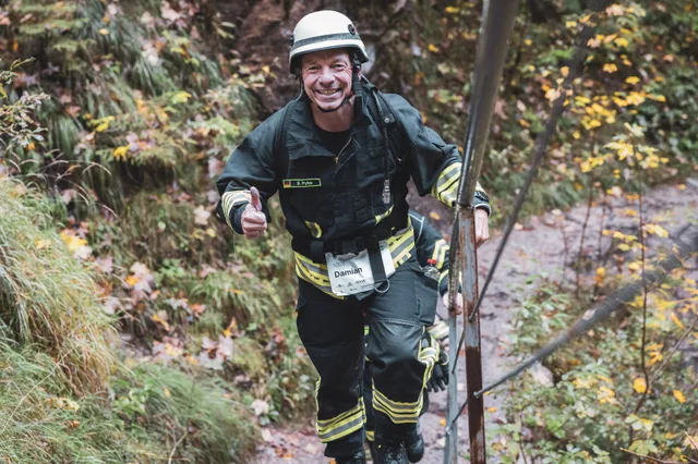 Lächelnder Teilnehmer in dunkler Einsatzkleidung auf den Waldstufen.
