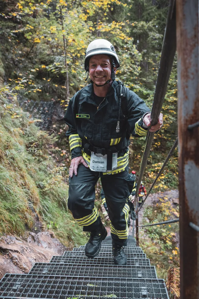 Lächelnder Teilnehmer in dunkler Einsatzkleidung auf den Waldstufen.