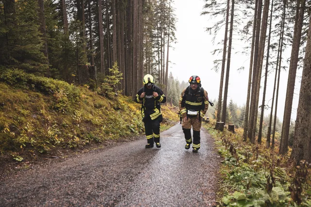 Zwei Teilnehmer mit Atemschutzgeräten steigen die Bergstraße im Herbstwald hinauf.