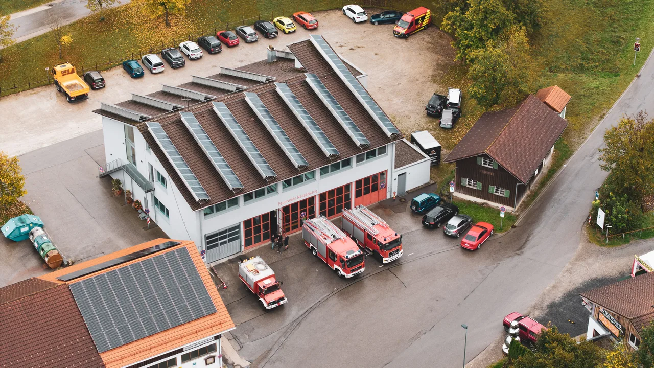 Luftaufnahme des Feuerwehrhauses Nesselwang mit Einsatzfahrzeugen und herbstlichen Bäumen.