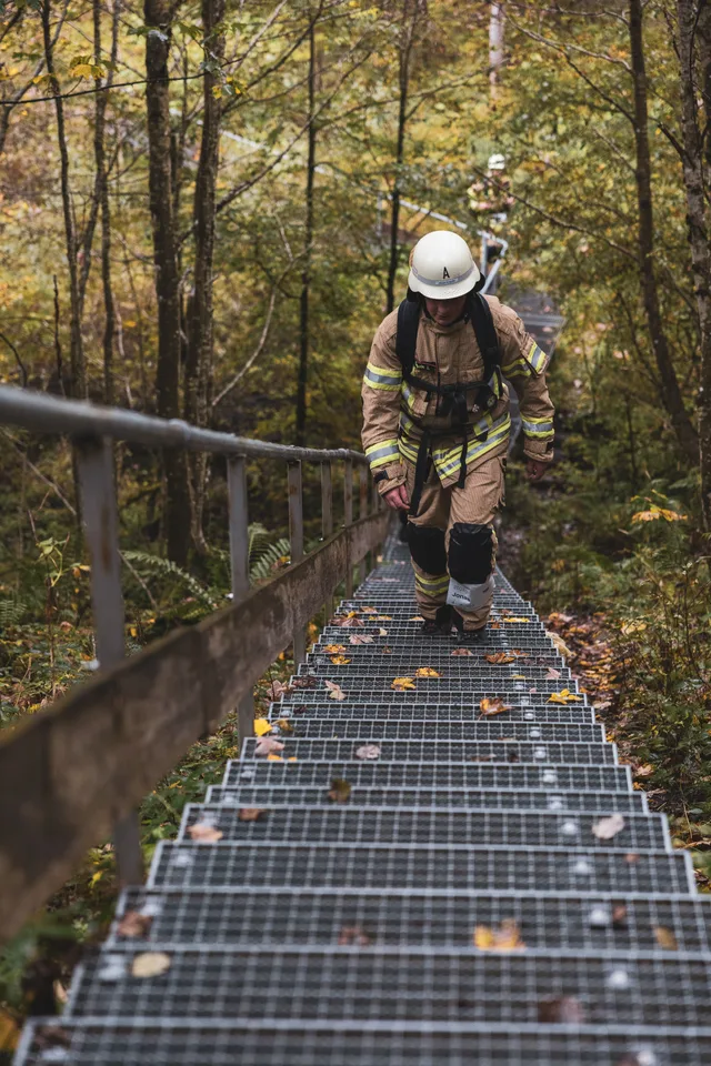 Teilnehmer mit weißem Helm und beiger Einsatzkleidung steigt eine lange Metalltreppe hinauf.