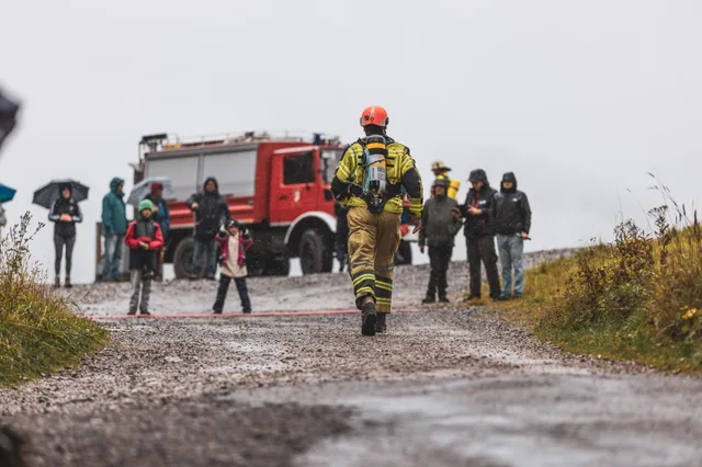 Teilnehmer mit orangefarbenem Helm läuft von hinten gesehen zum Ziel am Feuerwehrfahrzeug.