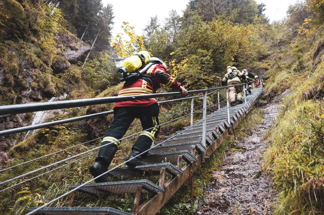 Teilnehmer in roter Einsatzkleidung mit gelber Atemluftflasche von hinten auf der Treppe.