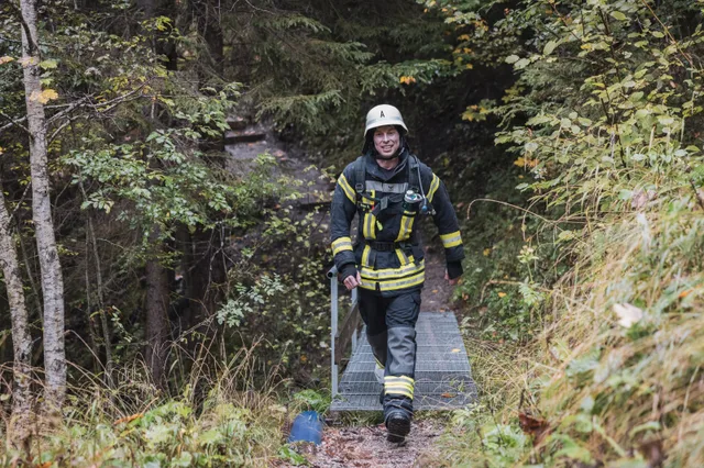 Lächelnder Teilnehmer mit grauem Helm und schwarzer Einsatzkleidung auf dem Waldweg.
