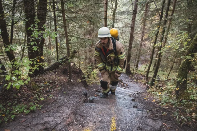 Teilnehmer mit weißem Helm und Atemschutzgerät auf steilen Waldstufen.