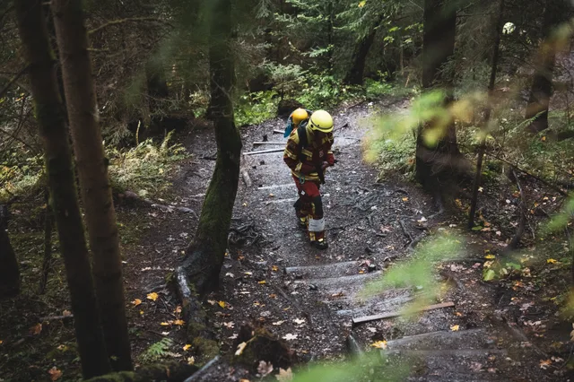 Teilnehmer in roter Einsatzkleidung beugt sich beim Aufstieg über die Waldstufen nach vorn.