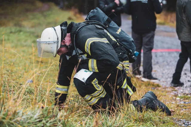 Teilnehmer kniet mit Atemschutzgerät im Gras neben der Strecke.