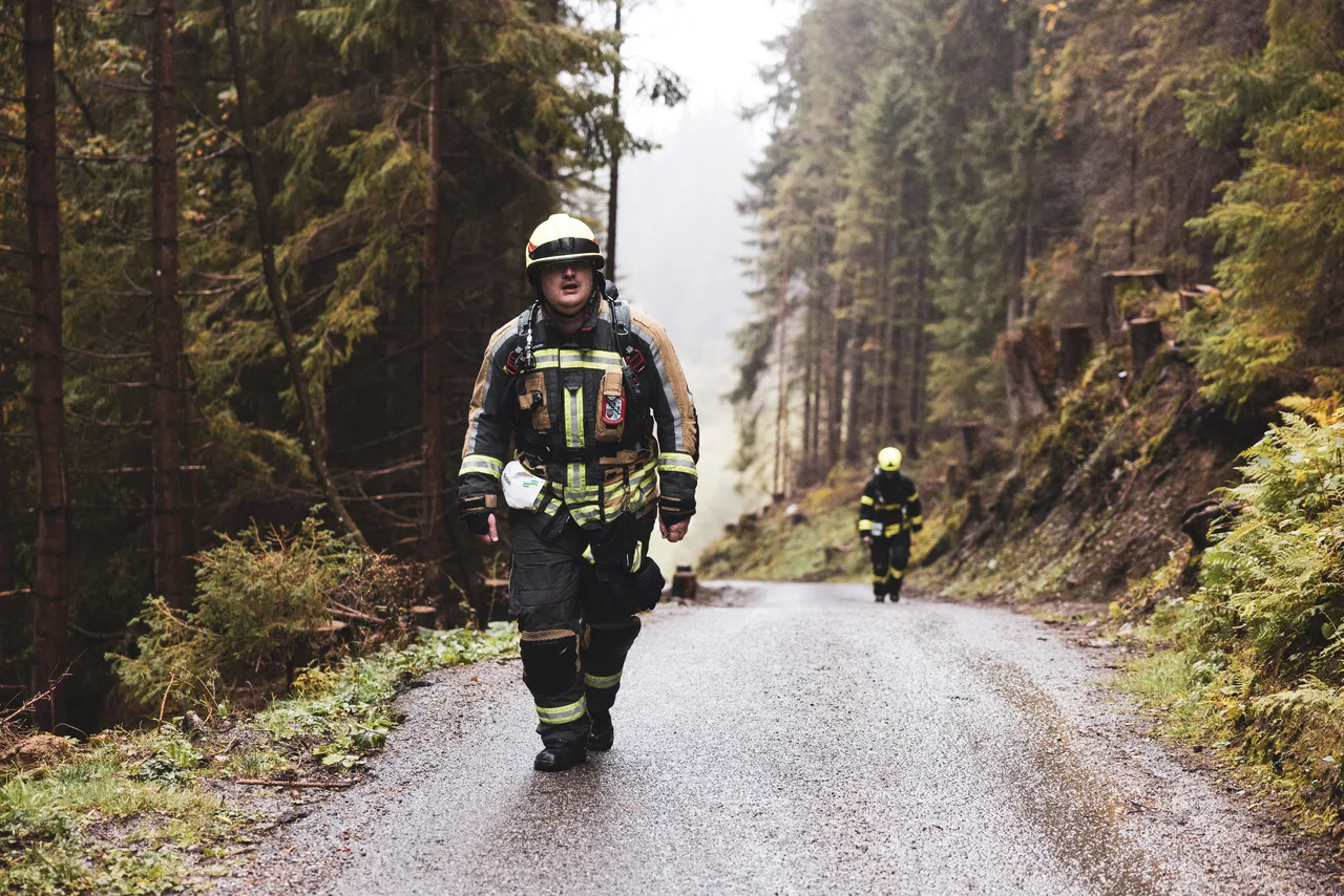Feuerwehrmann in Schutzkleidung steigt auf einer nassen Straße durch den nebligen Wald bergauf.