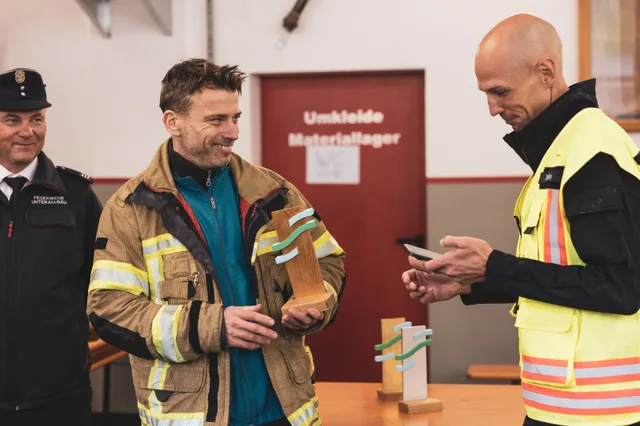 Teilnehmer in beiger Einsatzkleidung hält einen Pokal neben dem Organisator.