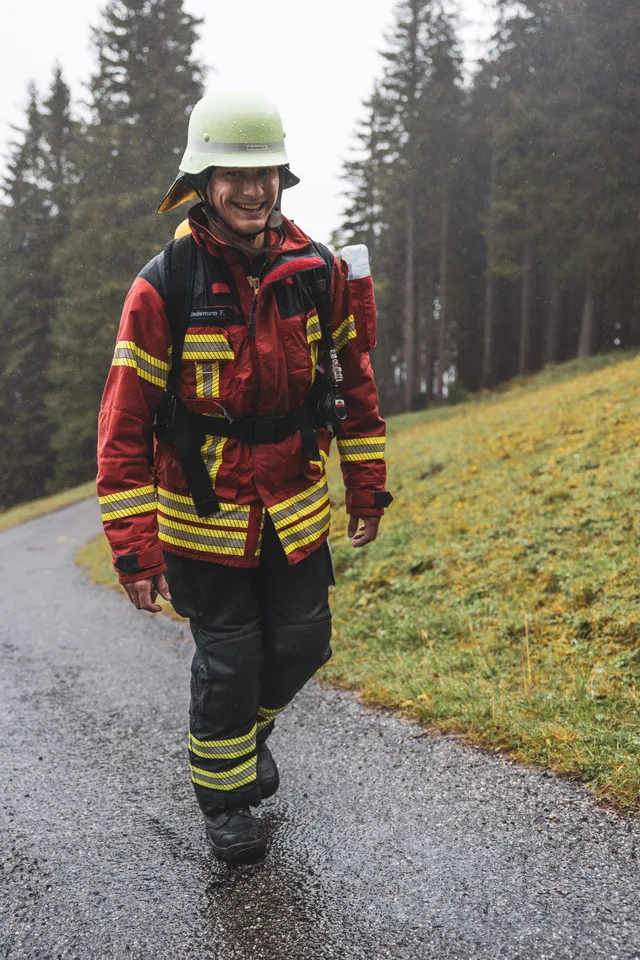 Teilnehmer in roter Einsatzkleidung und weißem Helm auf der nassen Bergstraße.