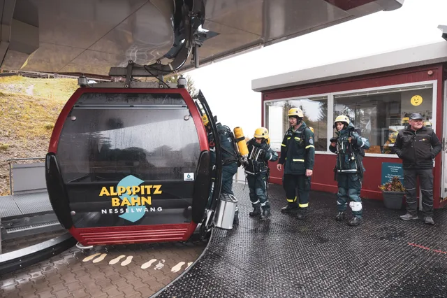 Teilnehmer in Einsatzkleidung steigen an der Bergstation in eine rote Gondel.