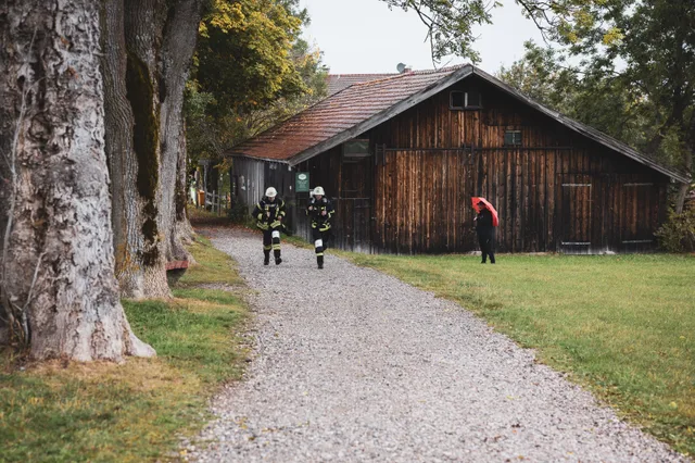 Zwei Teilnehmer in dunkler Einsatzkleidung neben einer Holzhütte im Wald.