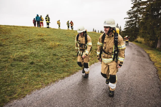 Zwei Teilnehmer in beiger Einsatzkleidung gehen auf der Bergstraße bergauf.