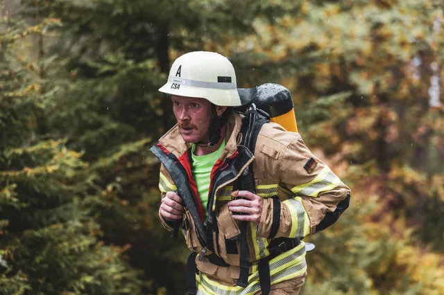 Feuerwehrmann mit weißem Helm hält beim Aufstieg im Regen beide Tragegurte seines Atemschutzgeräts.