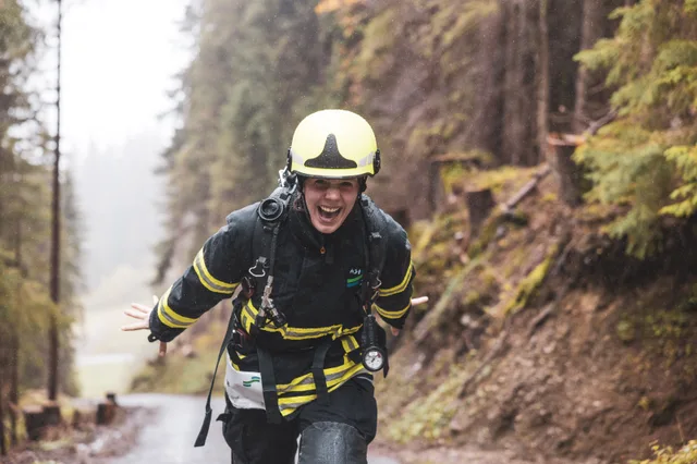 Lachende Teilnehmerin mit gelbem Helm und schwarzer Einsatzkleidung beim Aufstieg.