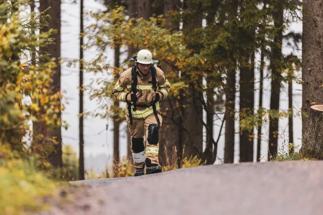 Teilnehmer mit weißem Helm und beiger Einsatzkleidung am Waldrand.