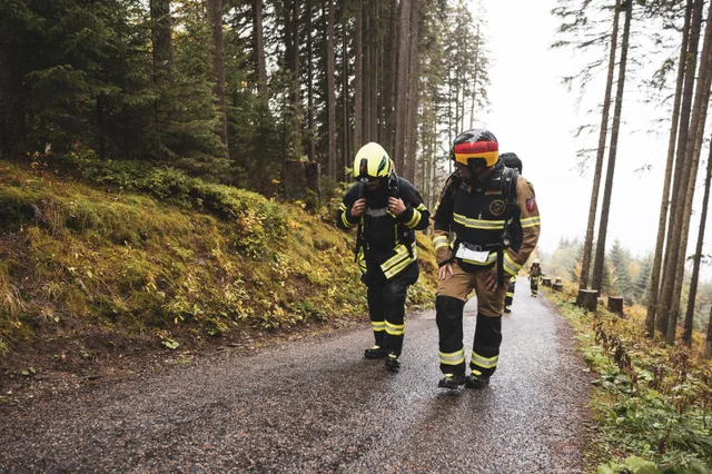 Zwei Teilnehmer mit Atemschutzgeräten steigen die Bergstraße im Herbstwald hinauf.
