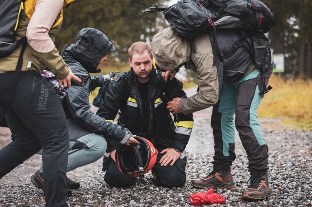 Teilnehmer sitzt auf dem Schotter, während andere ihm mit der Ausrüstung helfen.