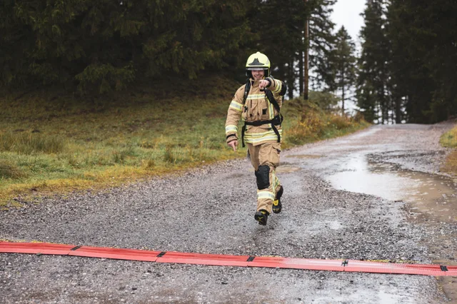 Teilnehmer mit gelbem Helm und beiger Einsatzkleidung überquert die Zielmarkierung.