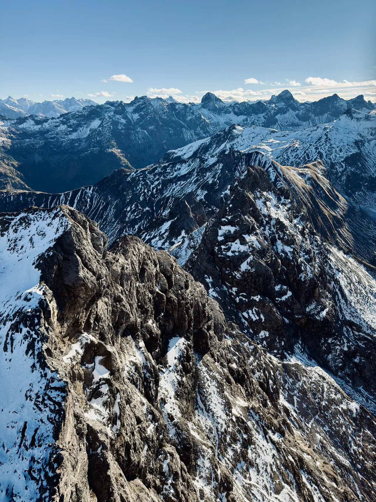 Schneebedeckte Felsgrate aus der Luft vor einer weiten Kette markanter Alpengipfel